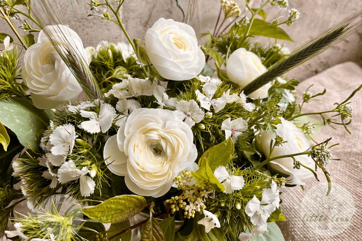 All-white funeral arrangement of ranunculus and dianthus with green rye grass